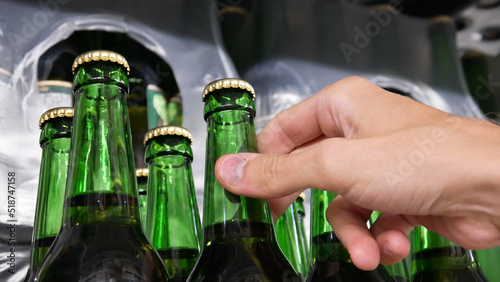 Close-up of many green glass bottles of beer on a store shelf and a male hand takes a one