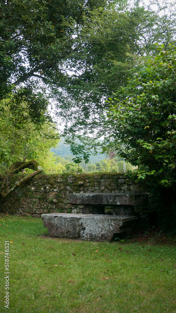 Banco y mesa de piedra junto a muro de piedras en jardín Banco y mesa de piedra junto a muro de piedras en jardín