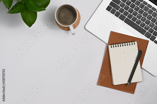 Simple workplace with laptop, notepad, coffee cup and houseplant on white table