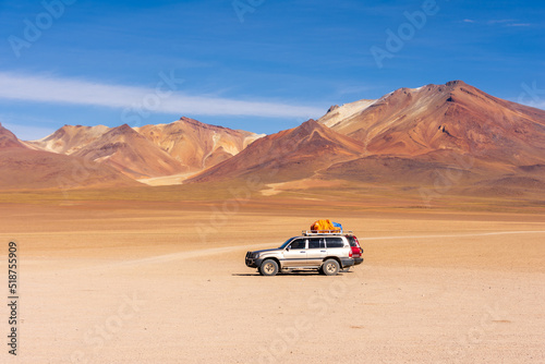 Two 4x4 cars wait in the Siloli desert with the colourful Andes in the background in the Altiplano region of Bolivia.