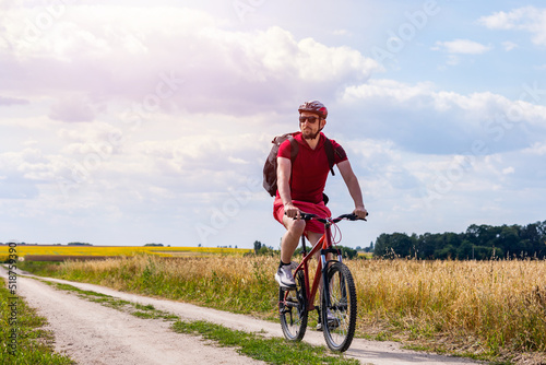cyclist in red t-shirt and shorts riding a bike in the countryside. man cycling in summer.