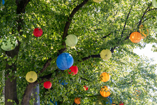 viele bunte Laternen wie Bälle hängen in den Zweigen der Baumkrone - rot blau gelb orange grün