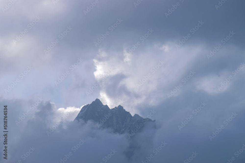 Incredible mountain massif covered with dense clouds during monsoon. Sun is hidden behind the clouds on a rainy day. A beautiful and amazing mountain landscape in Manali, Himachal Pradesh in India.