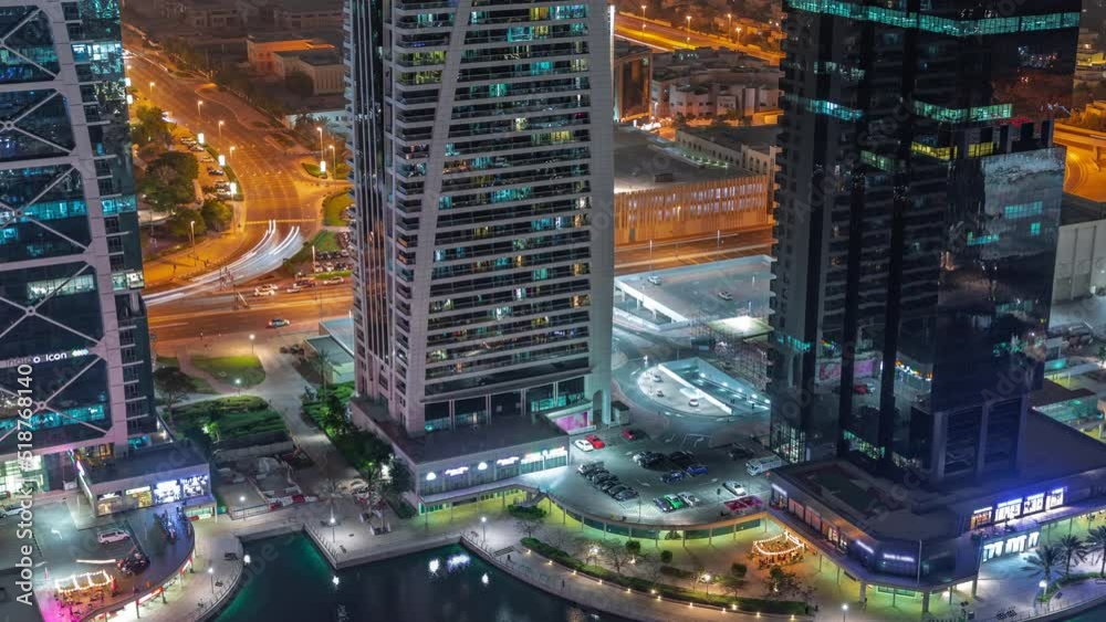 Tall residential buildings at JLT district aerial night timelapse, part of the Dubai multi commodities centre mixed-use district. Parking on intersection and car parking