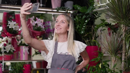 Beautiful girl takes a selfie photo in a flower shop. Florist worker with aprons in a flower shop posing for selfie photos for social networks
