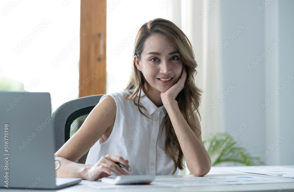 Charming Asian woman working at the office using a laptop Looking at the camera. Charming Asian woman working at the office using a laptop Looking at the camera.