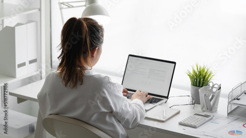 Rear view of businesswomen busy using laptop computer at office desk.