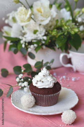 Red velvet cupcake with cream icing, decorated table detail with white flowers in the background