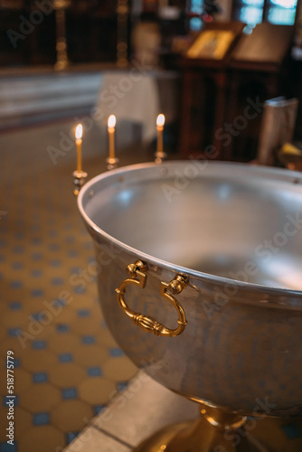 the baptismal cup is filled with water in the church, candles are burning, the l Fototapeta