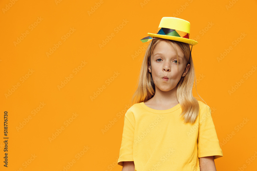 a cute, funny girl, of school age, stands on a yellow background in a yellow T-shirt in a straw hat. Horizontal studio photography with blank space for advertising mockup