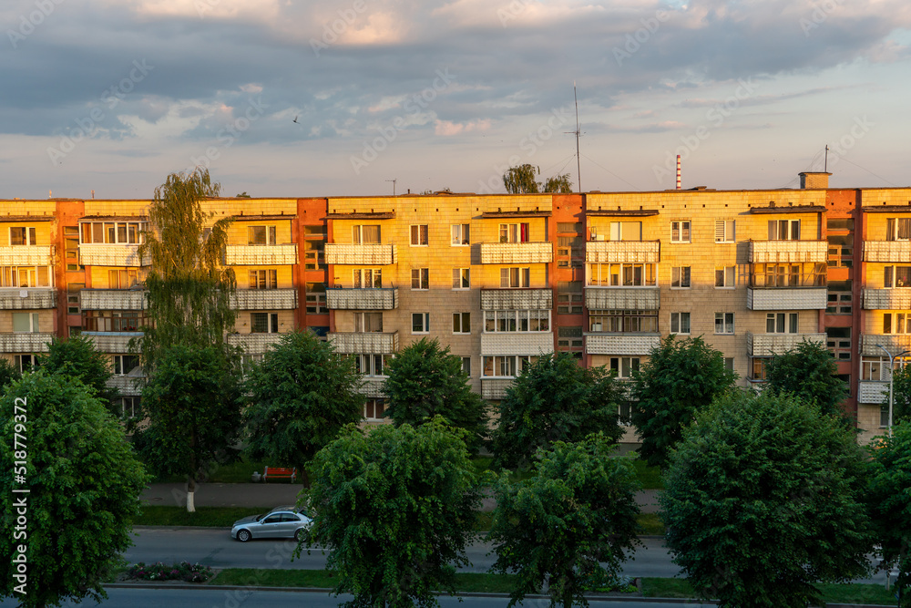 Panel residential building surrounded by greenery and trees. A green city in an ecologically clean area. The house is flooded with the orange light of the setting sun