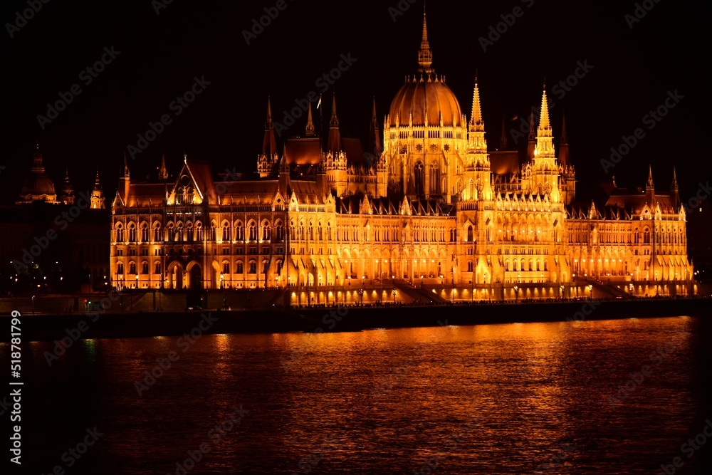 Panoramic night view of the Hungarian Parliament in Budapest at night. travel and tourism concept. calm smooth water surface of the Danube river. bright orange reflections. neo gothic style. 