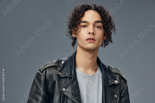 Pretty sexy self-confident stylish tanned curly man leather jacket posing isolated on over gray studio background. Cool fashion offer. Huge Seasonal Sale New Collection concept. Copy space for ad