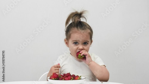 Cute little girl eats strawberries on a white background. Houses.
