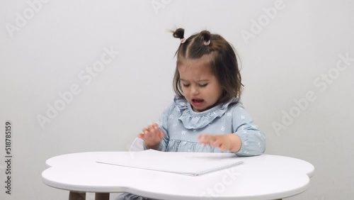 Capricious little girl at the table on a white background. Education.