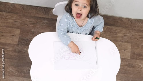 Flat. Cheerful child draws while sitting at the table at home