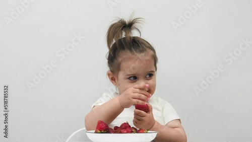 Funny little girl eats strawberries. On a white background.