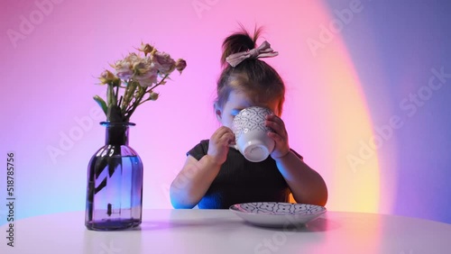 Cute little girl drinking tea while sitting at the table at home. Studio light.