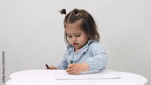 Cute little girl draws while sitting at the table at home. White background.