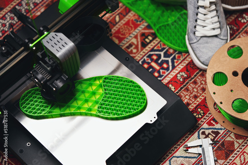 A shoe sole with distinct inner structure is printed from green filament on a 3D-printer with steel print bed. comfy home concept with persian rug, grey sneaker shoes and filament. selective focus photo