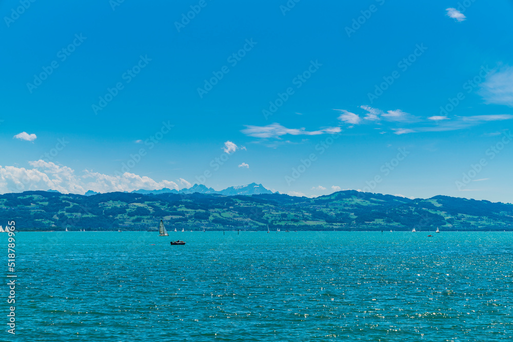 Germany, Bodensee panorama landscape view to snow covered saentis mountain peak nature and alps from water with many sailboats in summer with sun