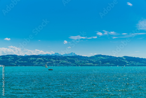 Germany, Bodensee panorama landscape view to snow covered saentis mountain peak nature and alps from water with many sailboats in summer with sun