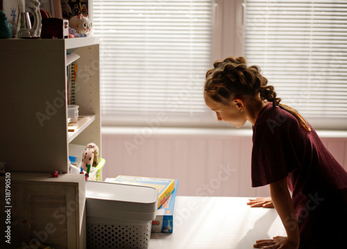 A cute small girl enjoying doing her distance education hometask and smiling while sitting alone at the table in a large guestroom at home. Homeschooling concept photo