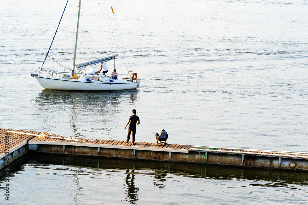 A sailing yacht is trying to moor at a pontoon pier. summer season