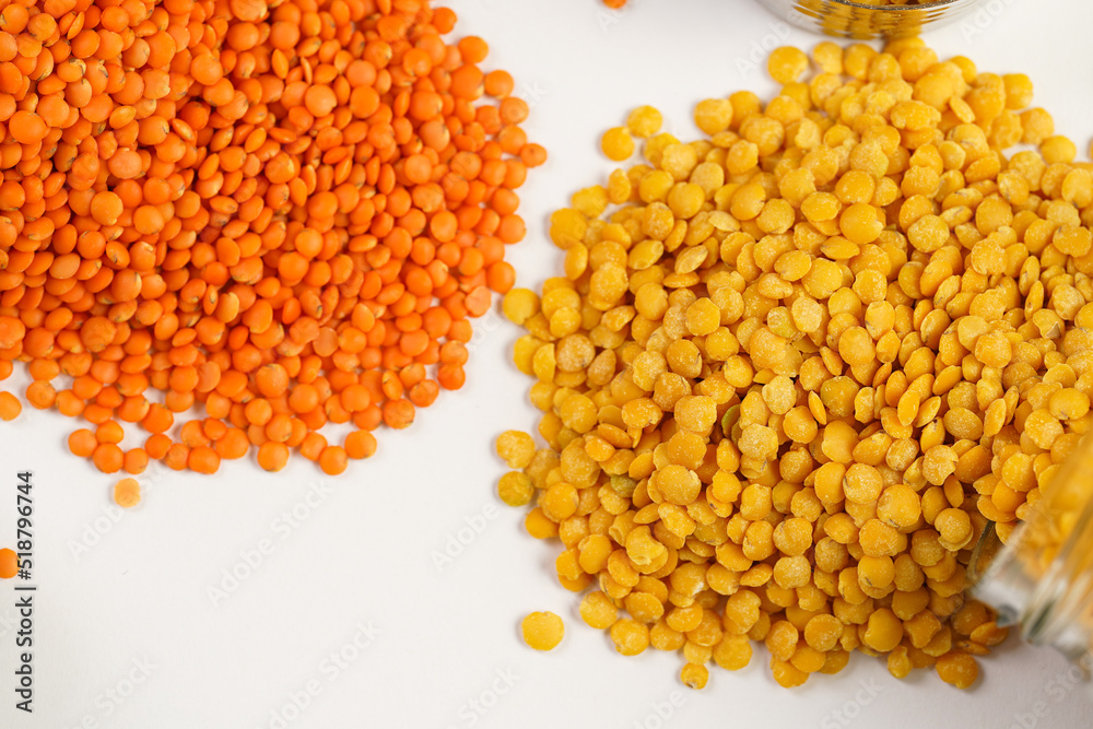a tall glass jar with dry red and yellow lentils tipped on the white table and a measuring cup with lentils a tall glass jar with dry red and yellow lentils tipped on the white table and a measuring cup with lentils