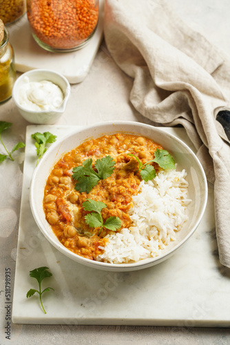 Indian red lentil curry with chickpeas, white rice and fresh cilantro - chana dal - in a white bowl on marble board