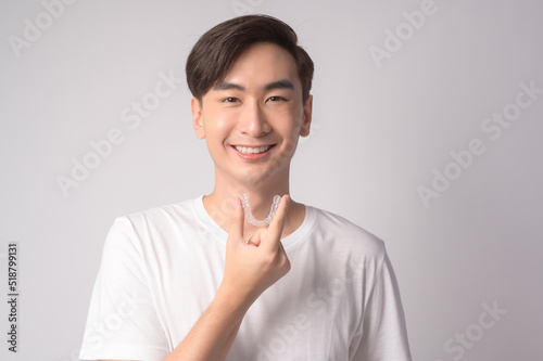 Young smiling man holding invisalign braces over white background studio, dental healthcare and Orthodontic concept..