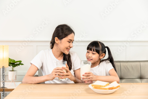 Asian family enjoying breakfast at living room. little girl daughter sitting on table, drinking milk with smiling father and mother in morning. Happy family at home.
