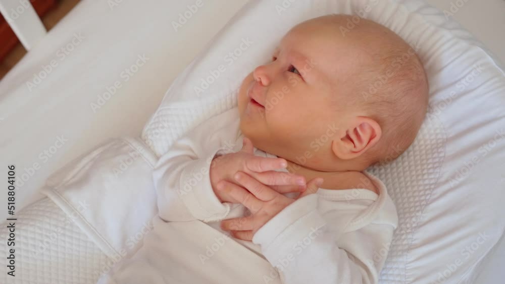 cute little newborn baby lies in a white crib in a cocoon for newborns, moves his arms funny and very cute, top view cute little newborn baby lies in a white crib in a cocoon for newborns, moves his arms funny and very cute, top view