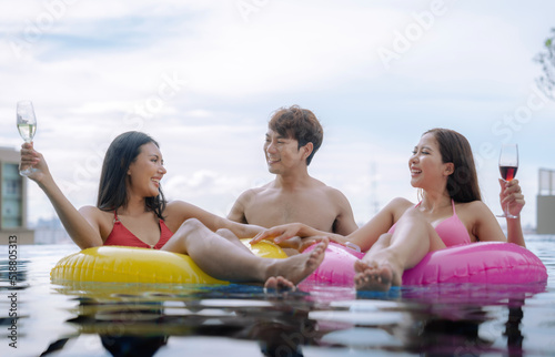 Group of friends relaxing on a floating beach mattress in a private pool at their villa.