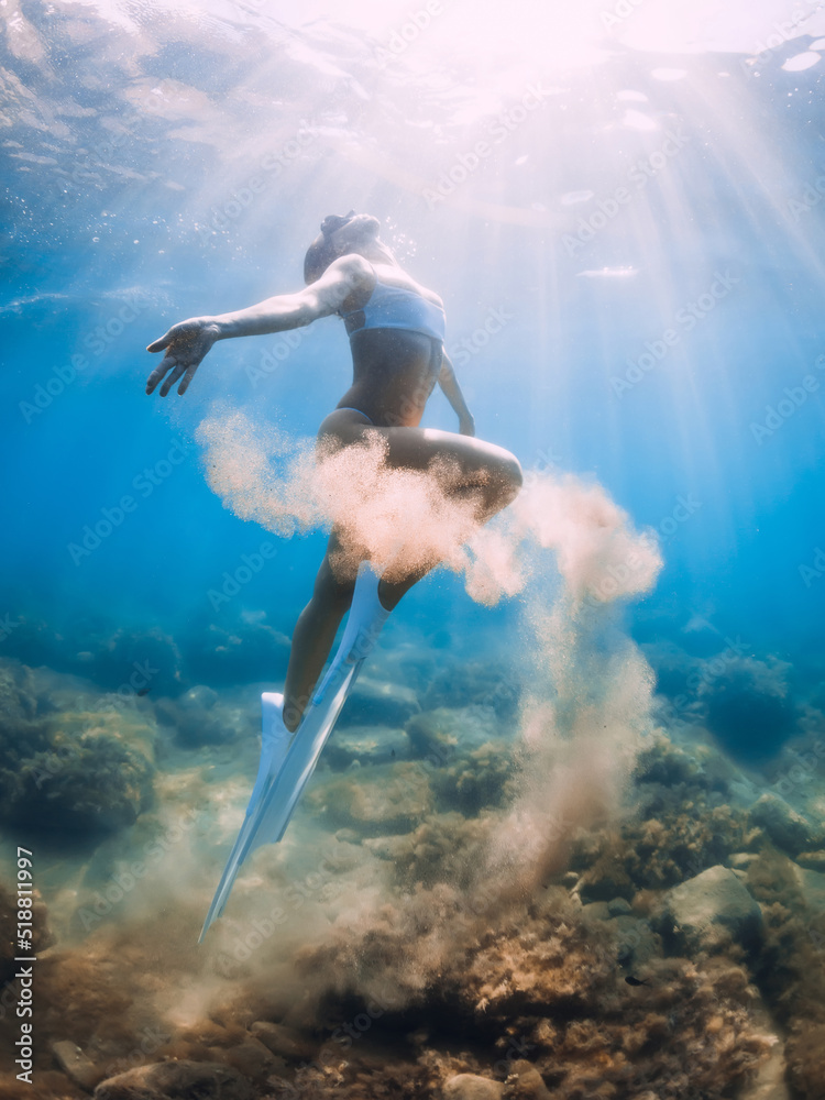 Freediver woman with sand in hands. Lady freediver with fins underwater in transparent ocean