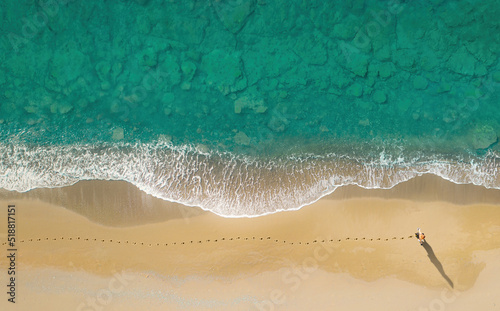 Woman walks on the beach along breaking waves leaving footprints on a sand. Aerial view directly above