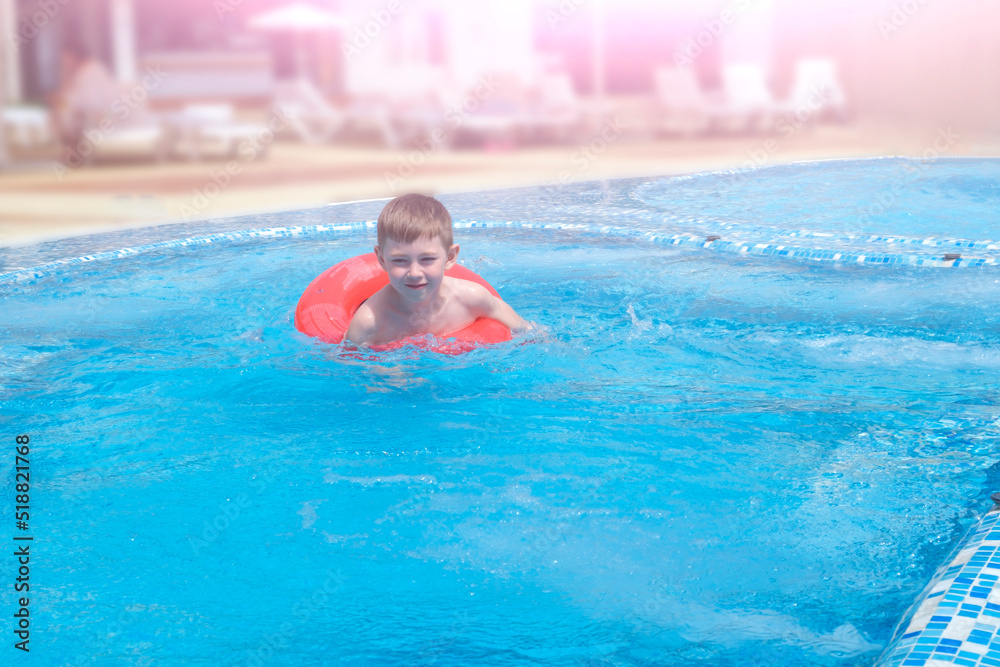 Little boy of 7 years swimming in pool with inflatable rubber ring. Funny happy child playing in aquapark. Summer holidays and vacation, travel and tourism concept.