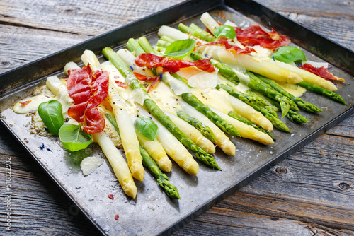 Traditioneller im Ofen überbackener weißer und grüner Spargel mit Käse und Sauce Hollandaise serviert als Draufsicht auf einem rustikalen Tablett photo