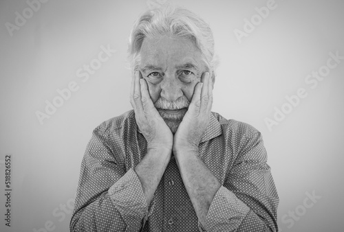 Black and white portrait of senior bearded man with hands over his face looking serious at camera