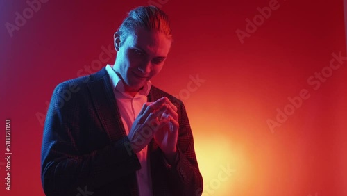 Evil plan. Exciting expectation. Coming soon. Neon light tricky sly smirking man waiting tenting fingers isolated on red orange color gradient copy space background.