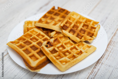 Freshly cooked Belgian waffles on a white plate on a light wooden background.
