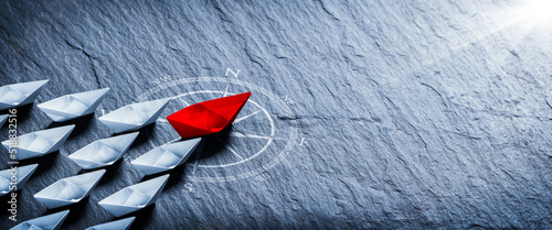Red Paper Boat On Compass Leading A Fleet Of Small White Boats - Business Leadership Concept photo