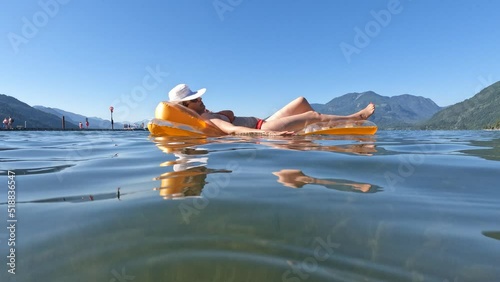 Mid adult woman lying on inflatable mattress, wearing a white straw sun hat that obscure her face while floating on the beautiful Harrison Lake surrounded with mountains in Harrison Hot Springs photo