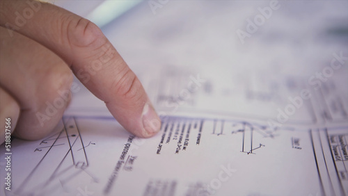 Close up view on engineer hand pointing at technical drawings. Men hands indicating some details in papers, blueprints with building project.