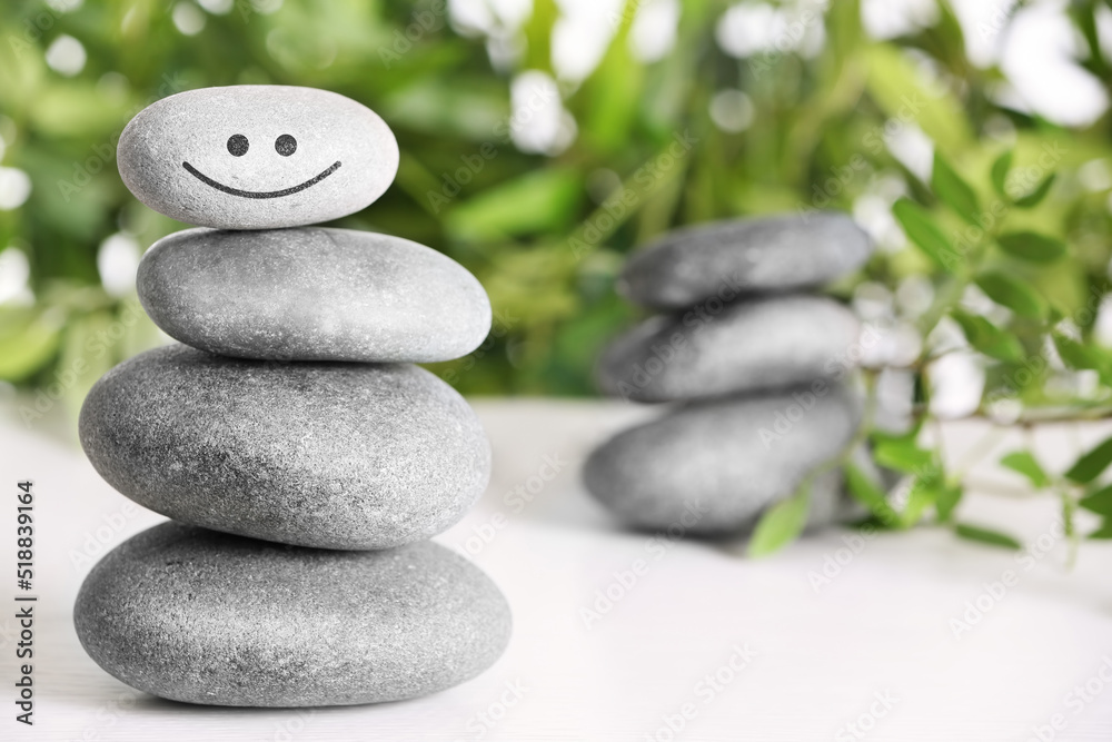 Stack of stones with drawn happy face on white table, space for text. Be in harmony and enjoying your life Stack of stones with drawn happy face on white table, space for text. Be in harmony and enjoying your life
