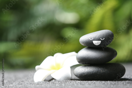 Stack of stones with drawn happy face and flower on grey table outdoors, space for text. Be in harmony and enjoying your life