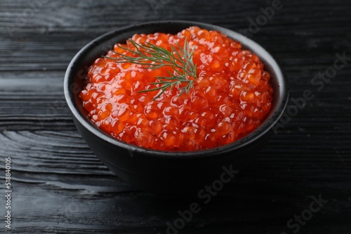 Bowl of delicious red caviar with dill on black wooden table