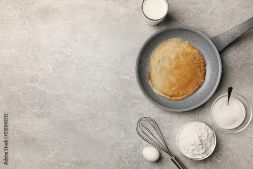 Frying pan with delicious crepe and ingredients on grey table, flat lay. Space for text