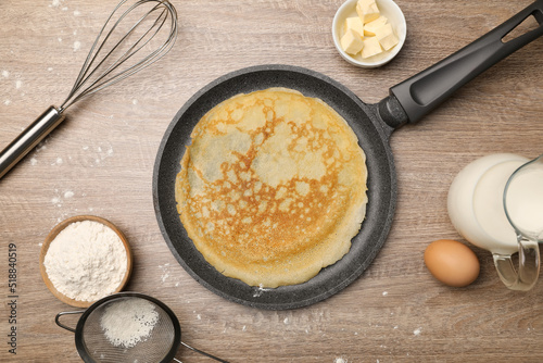 Frying pan with delicious crepe and ingredients on wooden table, flat lay photo