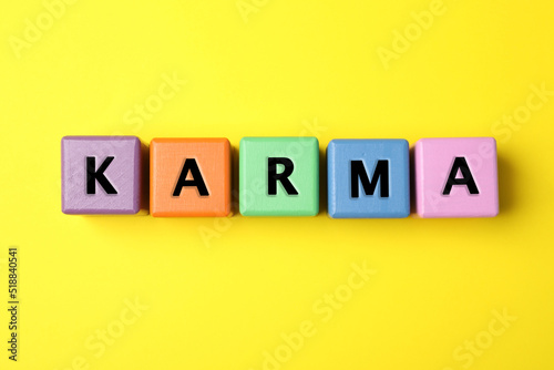 Word Karma made of colorful cubes with letters on yellow background, top view
